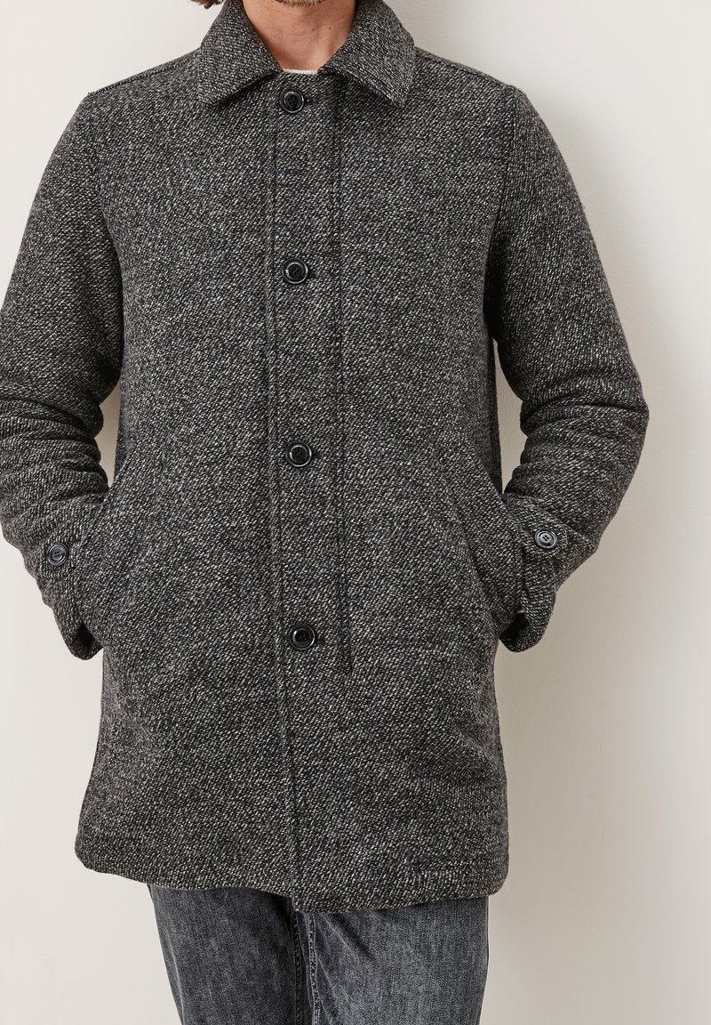 Abrigo gris de mezcla de lana con patrón de espiga, cuello vuelto, cierre frontal con botones y bolsillos laterales. Textura suave y ajuste entallado.