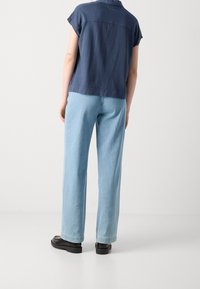 Chemise bleu marine à manches courtes avec des coutures discrètes, associée à un jean large bleu clair et des mocassins noirs. Fond neutre.