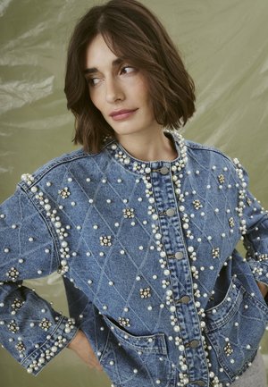 Giacca di jeans con motivo a rombi, arricchita da perle e strass. Chiusura con bottoni e tasche spaziose incluse.