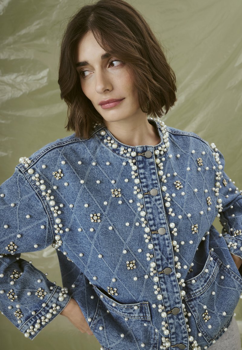 Denim jacket featuring a diamond pattern, embellished with pearls and rhinestones. Button closure and spacious pockets included.