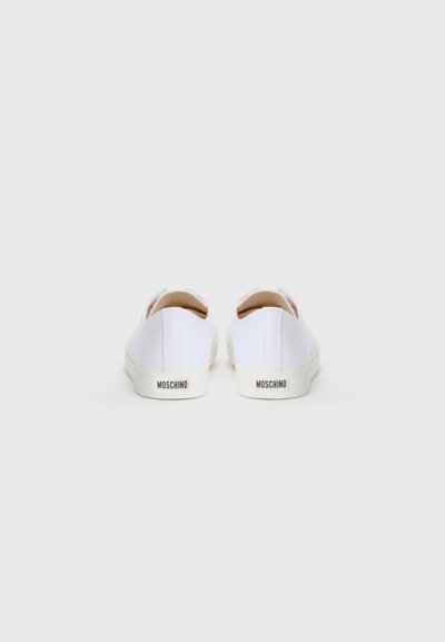 Bijele platnene slip-on tenisice s teksturiranom površinom, s kremastom gumom na potplatu i crnim "MOSCHINO" logotipom na peti.