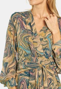 Wielokolorowa sukienka kopertowa z lekkiej tkaniny, z wirującym wzorem w odcieniach niebieskiego, zielonego i burgundowego. Wyraźnie zaznaczona talia, z długimi rękawami.