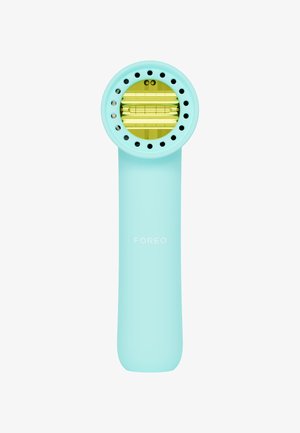Helles blaues Gesichtspflegegerät mit einem runden Kopf, der gelbe Akzente und Löcher für die Luftzirkulation aufweist. Glatter Griff, markiert mit dem "FOREO"-Logo.