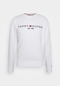 Bílá mikina s dlouhými rukávy. Má logo „TOMMY HILFIGER“, červené a modré akcenty a žebrované manžety a spodní lem. Hladká texturovaná látka.
