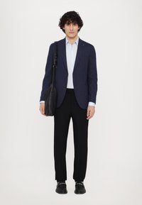 Marineblauwe gestreepte blazer over een lichtblauw shirt, Zwarte broek, met een zwarte leren tas en zwarte schoenen. Modern, op maat gemaakt.