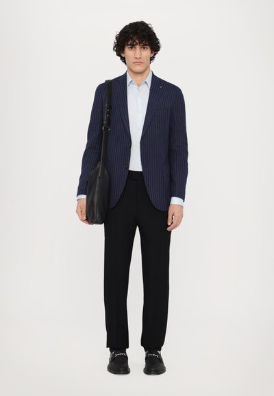 Blazer bleu marine à rayures verticales porté sur une chemise bleu clair, avec un pantalon noir, un sac en cuir noir et des chaussures noires. Moderne, coupe ajustée.
