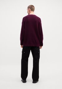 Dark purple knit sweater with a relaxed fit, ribbed texture, and a wide neckline, paired with black cargo pants featuring side pockets.