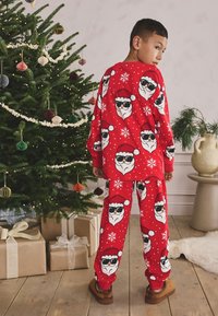 Ensemble de pyjama rouge avec de grands imprimés de visage du Père Noël portant des lunettes de soleil. Tissu doux, haut à manches longues et pantalon assorti. Accents de flocons de neige blancs.