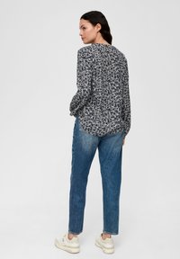 Druckbluse in Navy mit weißen Akzenten, Rundhalsausschnitt und langen Ärmeln. Kombiniert mit hellblauen, lässig geschnittenen Jeans und beigen Turnschuhen.