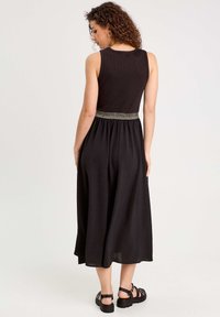 Robe noire sans manches avec un corsage côtelé et une jupe froncée. Présente une taille accentuée en or. Texture lisse, design longueur cheville.