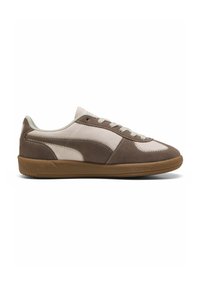 Zapatilla marrón y beige con una textura suave, punta redonda, diseño con cordones y suela de goma; presenta un distintivo detalle de raya lateral.