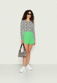 T-shirt de mangas longas com riscas de zebra brancas e pretas, combinada com calções verdes brilhantes. Acessórios com uma bolsa com padrão de zebra e sapatilhas brancas.