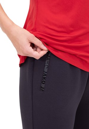 Rode sporttop met korte mouwen, gecombineerd met donkerblauwe broek met een verticale zwarte logo-accent bij de zak.