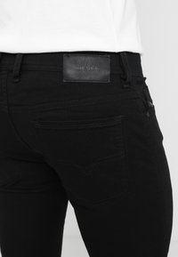 Svarta denimjeans med en läderpatch där "DIESEL" är präglat. Synlig söm i en subtil design på bakfickorna.