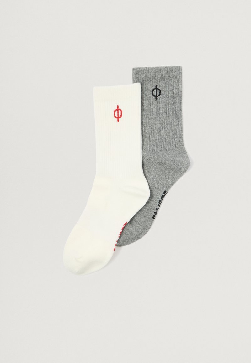 Du išsiskiriančių šilkinių kojinių poros: vienos baltos su raudonu logotipu, kitos pilkos su juodu logotipu. Abi yra iki blauzdų ilgio ir pagamintos iš minkštos medžiagos.