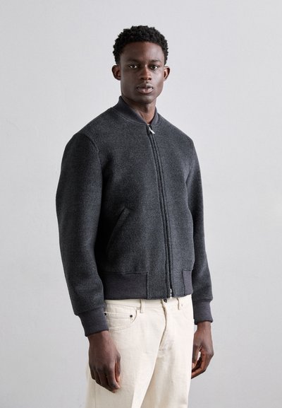 Veste bomber en laine grise avec fermeture éclair sur le devant, poignets et taille côtelés, et poches latérales. Texture lisse, design minimaliste.