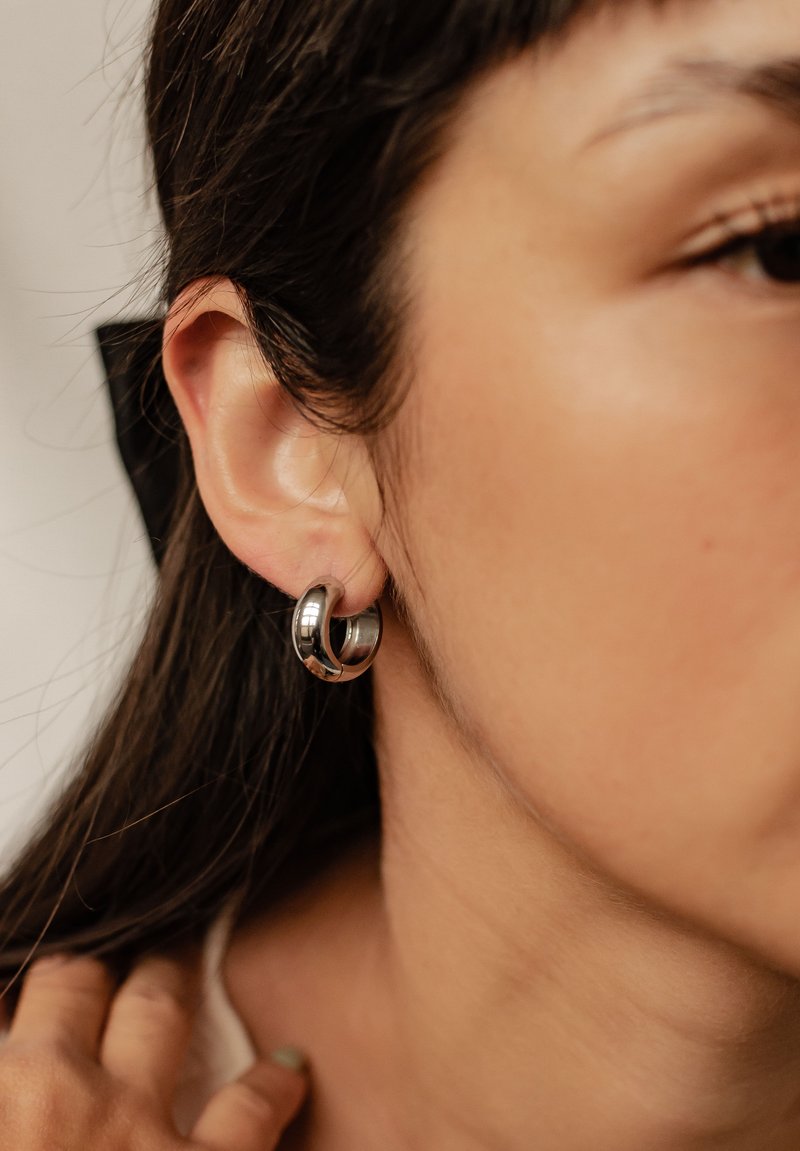 Orecchini a cerchio in argento con una finitura lucida, caratterizzati da un design a doppio anello. Gli orecchini si posano sull'orecchio di un modello, evidenziandone la forma.