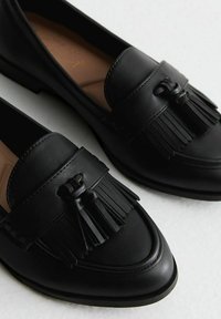 Zwarte leren loafers met een decoratieve franjerand en strikdetail aan de voorkant. Glad oppervlak met een ronde neus en een lage hak.