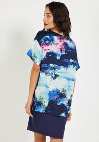 Top de manga corta con un estampado abstracto multicolor en azul, rosa y verde; corte holgado con un escote redondeado y dobladillo inferior azul marino.