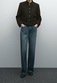 Brown textured jacket with gold buttons and two front pockets, paired with light to dark wash wide-leg jeans and black footwear.