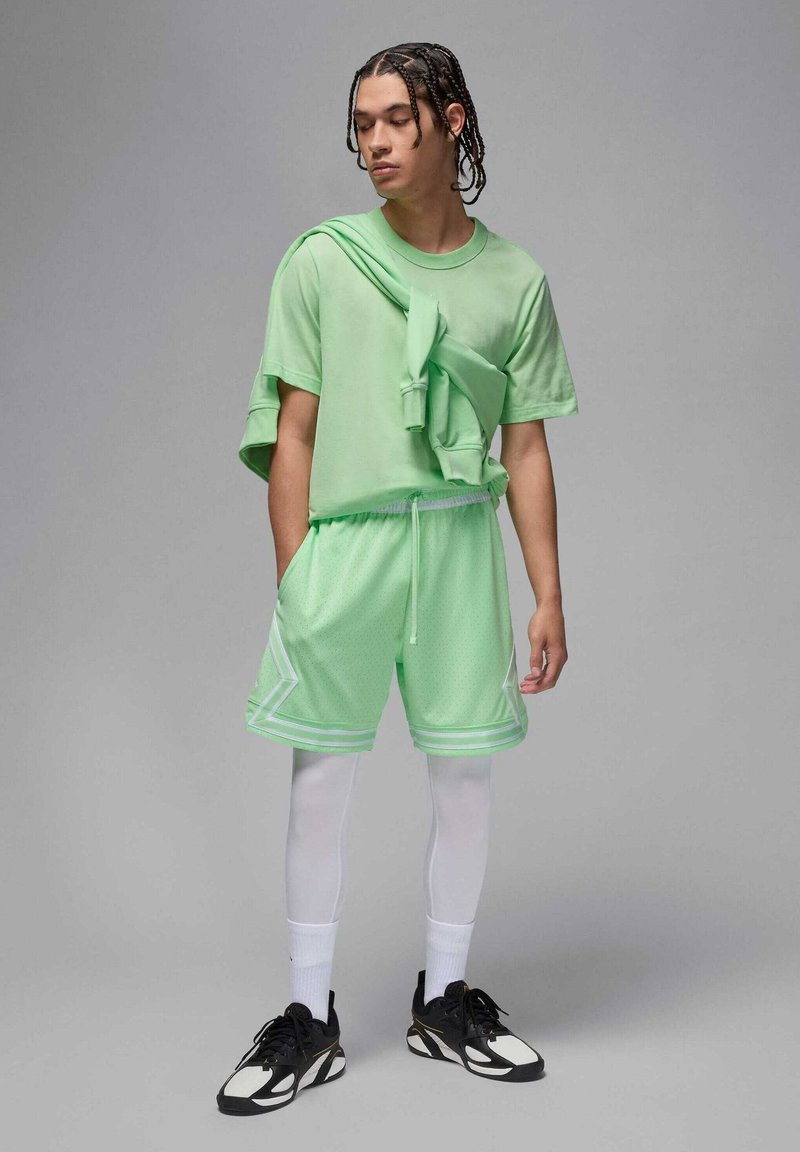 Camiseta oversized color verde menta con mangas cortas, estilizada con una sudadera con capucha encima. Pantalones cortos de malla liviana con acentos blancos en contraste.