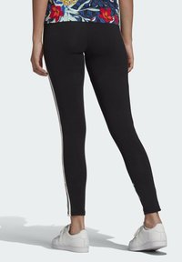 Černé legíny s úzkým střihem, se bílými postranními pruhy. Vyrobené z elastické látky, navržené pro pohodlí a pohyblivost.