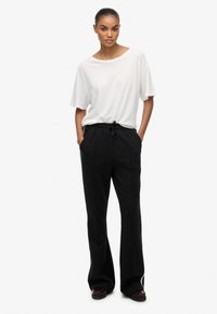 Camiseta blanca de corte holgado con un escote amplio, combinada con pantalones negros de cintura alta con cordón en la cintura y perneras acampanadas.