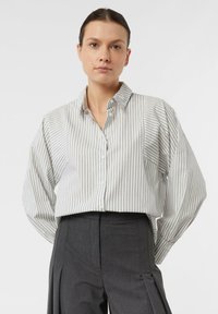 Striped button-up shirt in light gray and white cotton, featuring a collar and loose sleeves, paired with tailored dark gray trousers.