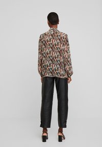 Langemouw blouse met een multikleuren bloemenpatroon, lichte stof, losse pasvorm en met knopen sluitende mouwen. Gekleed met zwarte leren broeken.