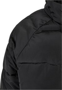 Chaqueta acolchada negra con un alto cuello y secciones acolchadas. El material parece suave y brillante, mostrando un diseño minimalista sin adornos.