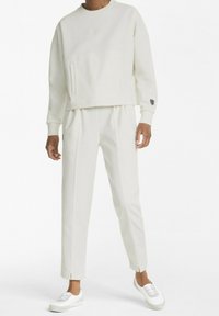 Vit kortärmad tröja med framfickor och ribbade muddar, i kombination med smala vita byxor med sidosömmar och matchande sneakers.