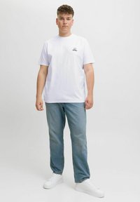 Hvid bomulds t-shirt med et lille sort grafisk motiv på brystet, parret med lyseblå denim jeans og hvide sneakers.