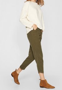 Crème gebreide trui met een ontspannen pasvorm, olijfgroene tapered broek en bruine suède enkellaarzen met ribbelstructuur.