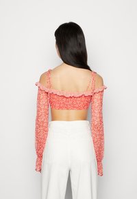 Top curto floral vermelho com mangas bufantes caídas, alças delicadas e um tecido estampado. Combinado com calças brancas de cintura alta.