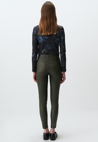 Olijfgroene, hoogopgetrokken skinny broek met een gladde textuur en achterzakken, gedragen met een lange mouw, bedrukte top.