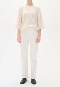 Suéter de punto de color beige claro y de gran tamaño, con mangas cortas, combinado con jeans blancos de pierna recta y zapatos negros sin cordones. Diseño simple y minimalista.