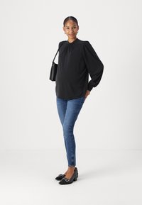 Black long-sleeve blouse with a gathered neckline, paired with blue skinny jeans and black pointed-toe flats featuring decorative hardware.