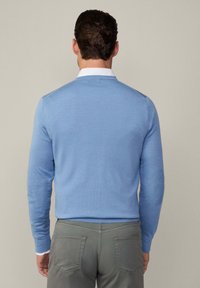 Hellblauer Pullover mit langen Ärmeln, geripptem Halsausschnitt und Saum. Verfügt über ein strukturiertes Strickmuster und Ellenbogenpatches. Wird mit grauen Hosen getragen.
