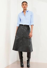 Sinine triibuline nööpidega särk, mille varrukad on üles keeratud, koos musta nahast A-lõikega seeliku ja põlvini ulatuvate mustade kontsakingadega.