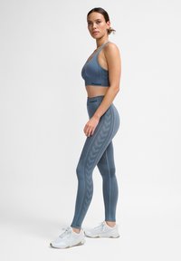 Sportset in Blau-Grau mit einem Sport-BH mit breiten Trägern und hochgeschnittenen Leggings mit strukturierten Mustern. Inklusive weißen Sneakers.