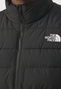 Närbild av en person som bär en svart puffjacka med dragkedja fram och The North Face-logotyp på bröstet.