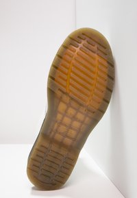 Suela de goma con una superficie texturizada y con patrón; huella hexagonal marrón para agarre; marca en relieve e información de seguridad cerca del talón.