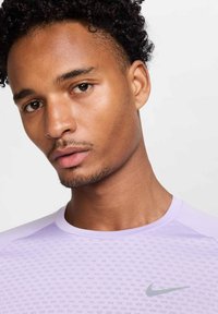 Light purple Nike athletic shirt with a textured pattern, featuring a round neckline and short sleeves. Small silver logo on chest.