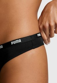 Schwarze Stringunterwäsche mit weichem elastischem Bund, der mit weißem "PUMA"-Branding versehen ist. Glattes Material und eine enganliegende Passform für hohen Tragekomfort.
