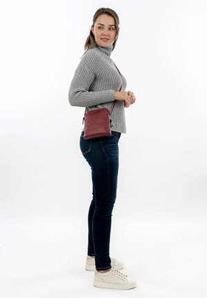 Small burgundy leather crossbody bag with a sleek design and adjustable strap, paired with a gray ribbed sweater and dark jeans.