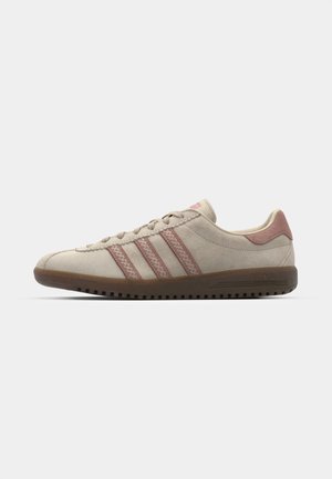 Beige suede sneaker with pink accents, featuring three overlapping stripes, a textured toe cap, and a rubber outsole with grooves.