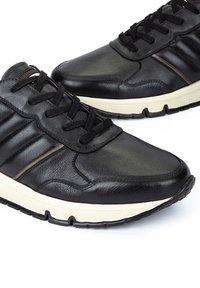 Baskets en cuir noir avec une finition lisse, des côtés texturés, des lacets noirs et une semelle en caoutchouc couleur crème. Présente des accents bruns discrets.