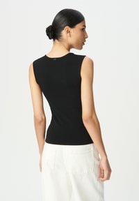 Top negro sin mangas con un diseño ajustado. Tela suave y elástica con un escote redondo. Combinado con pantalones blancos de cintura alta.