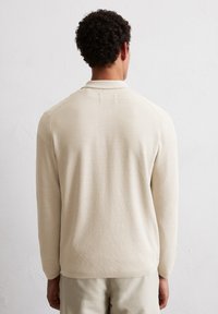 Jasnobeżowy sweter dzianinowy z teksturowanym wzorem, z kołnierzem i długimi rękawami, widok z tyłu. Gładki, miękki materiał.