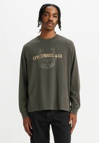 Oliwkowa koszula z długim rękawem i okrągłym dekoltem, z grafiką logo w jasnym beżu. Wykonana z miękkiego materiału, w luźnym kroju.